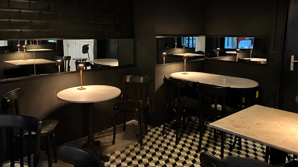 Stilvoll eingerichteter Gastraum mit dunklen Wänden, Marmortischen, geometrischem Bodenmuster und schmalen Tischleuchten.