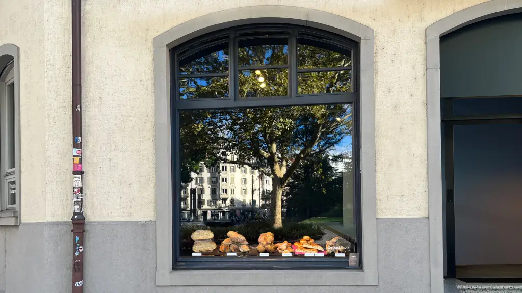 Schaufenster mit Brotauslage und sichtbarem Schriftzug bread.love unten rechts, Spiegelung von Baum, Häusern und Autos im Glas.